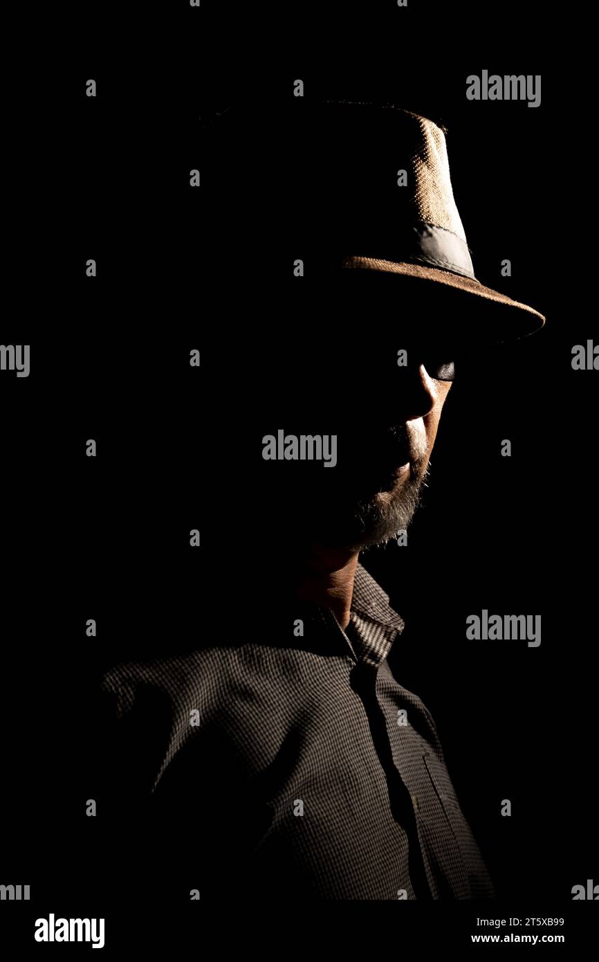 Discreet portrait of detective man with hat in darkness. Dark room art. Stock Photo