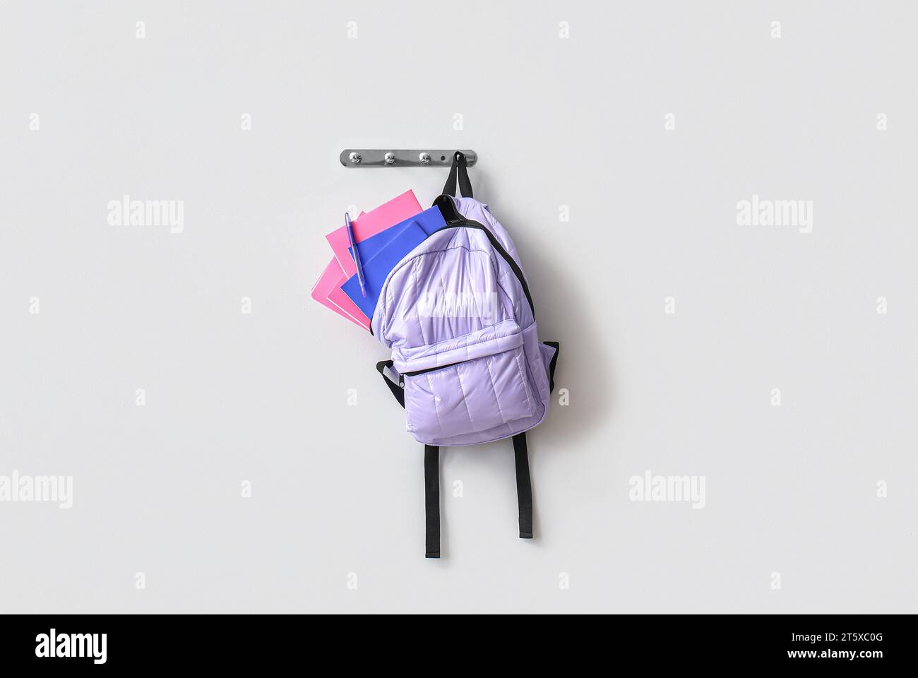 School backpack with stationery hanging on light wall Stock Photo
