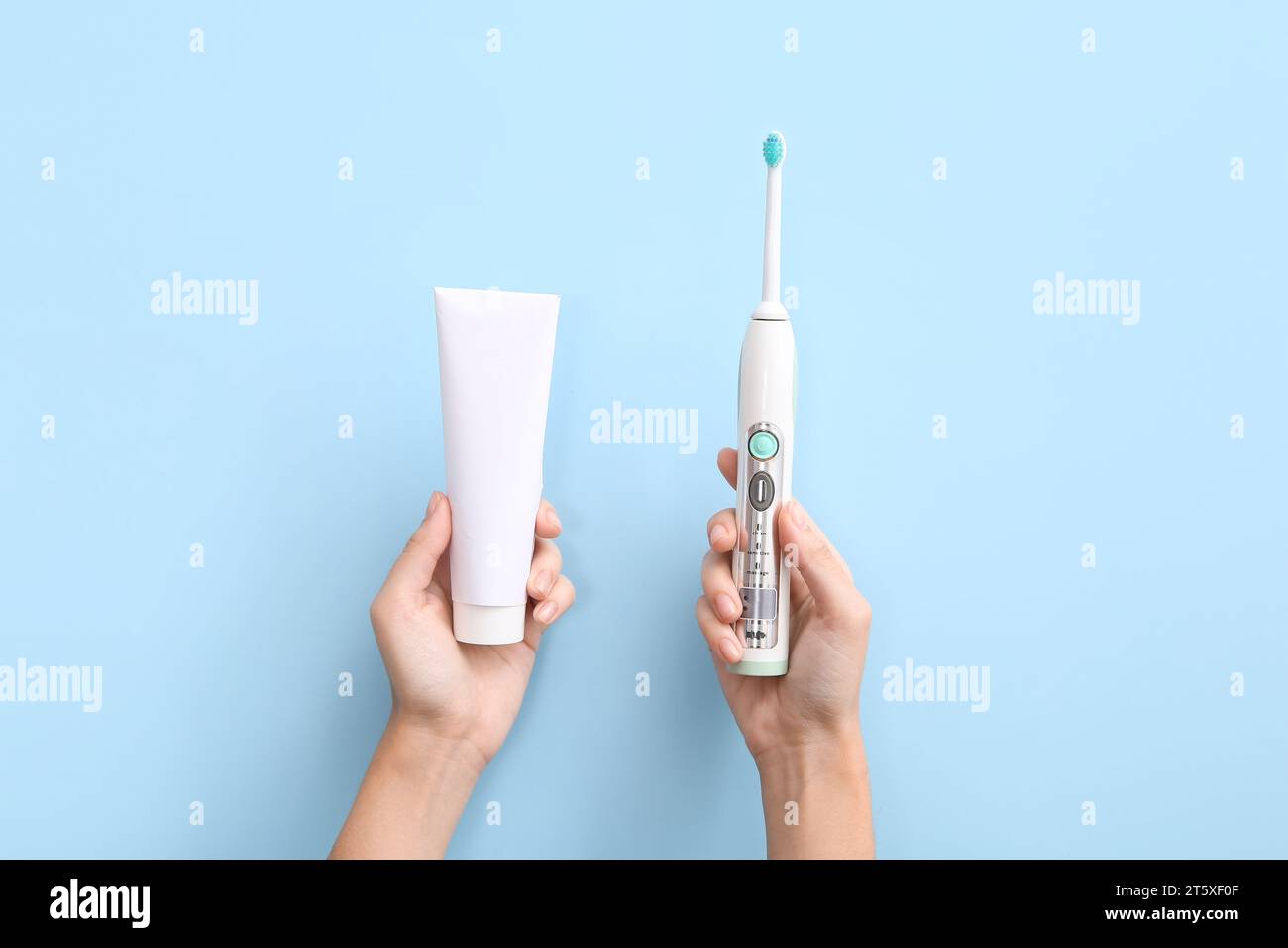 Female hands with electric toothbrush and toothpaste on blue background ...