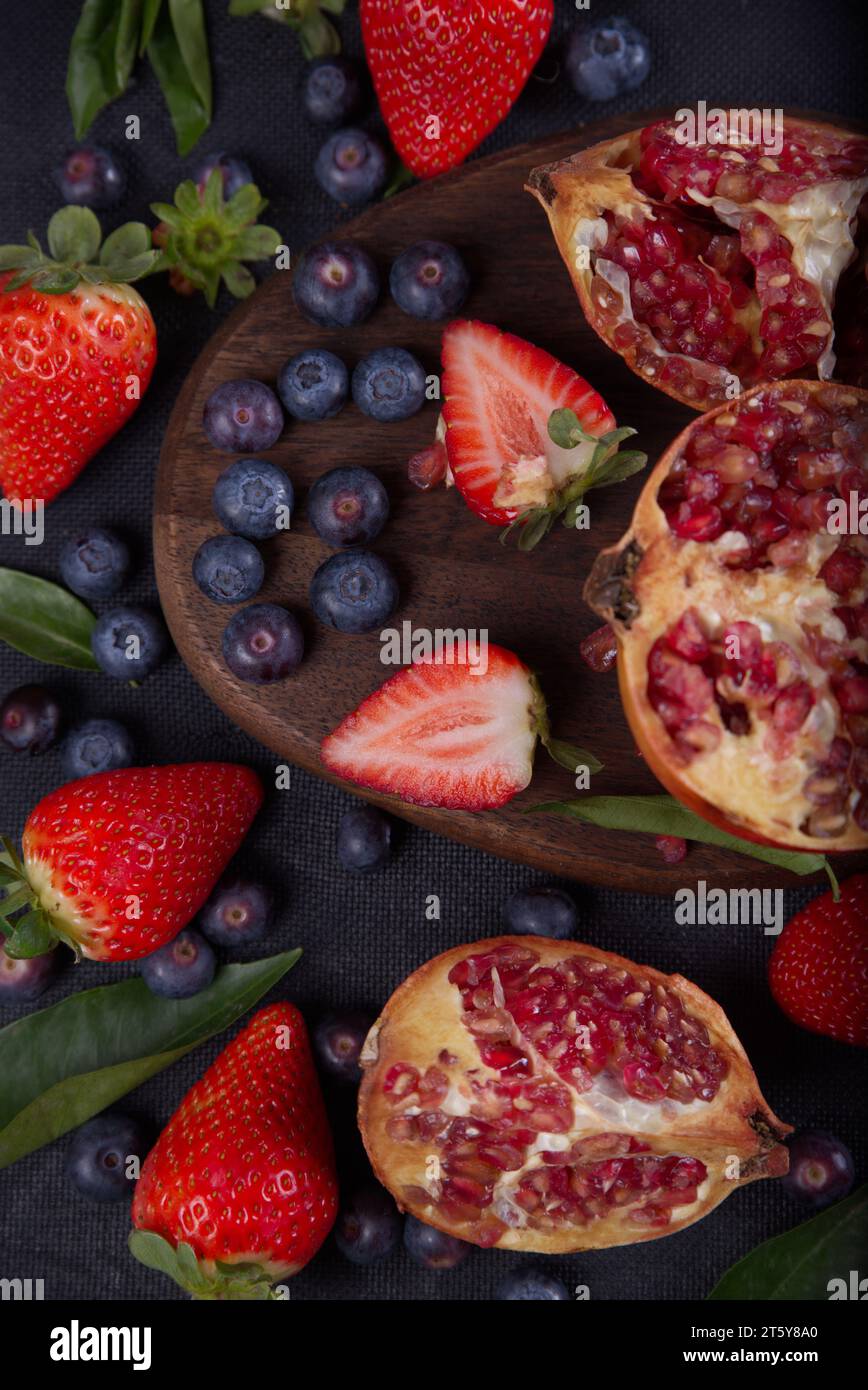 Strawberries, blueberries and pomegranates exposed on a wooden board in dark background. Stock Photo