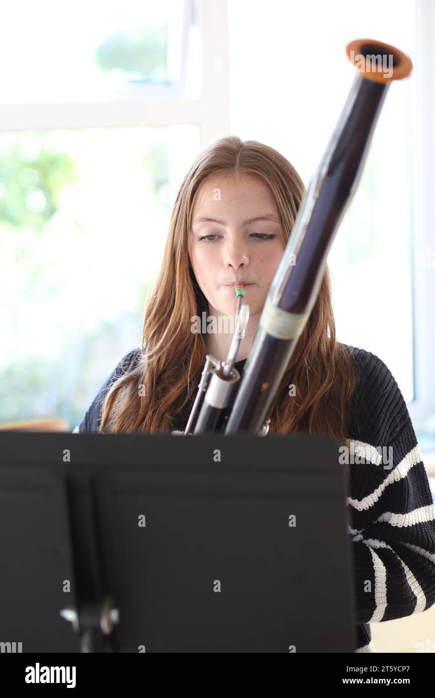 Teenage girl playing the bassoon in kitchen at home. Plays musical