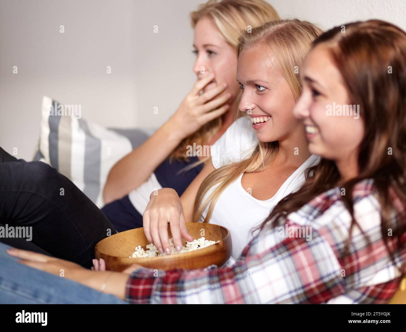 Watching movie, home and friends with popcorn, comedy and funny with humor, snack and bonding together. People, girls and women with cinema, treat and Stock Photo