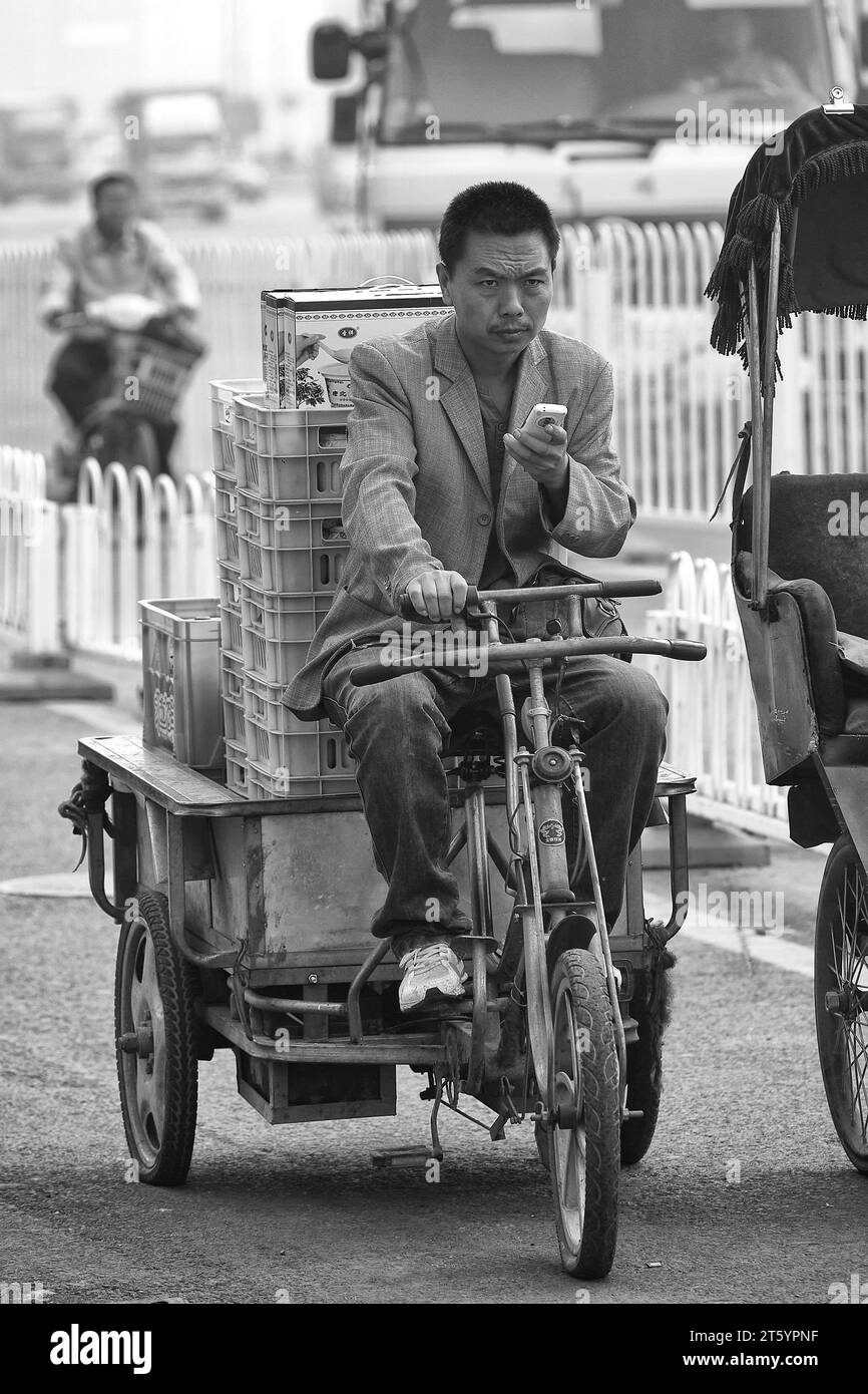Black And White Photo Of A Chinese Man Riding A Cycle Rickshaw (Three Wheeler) During The Morning Rush Hour, Beijing, China. Stock Photo