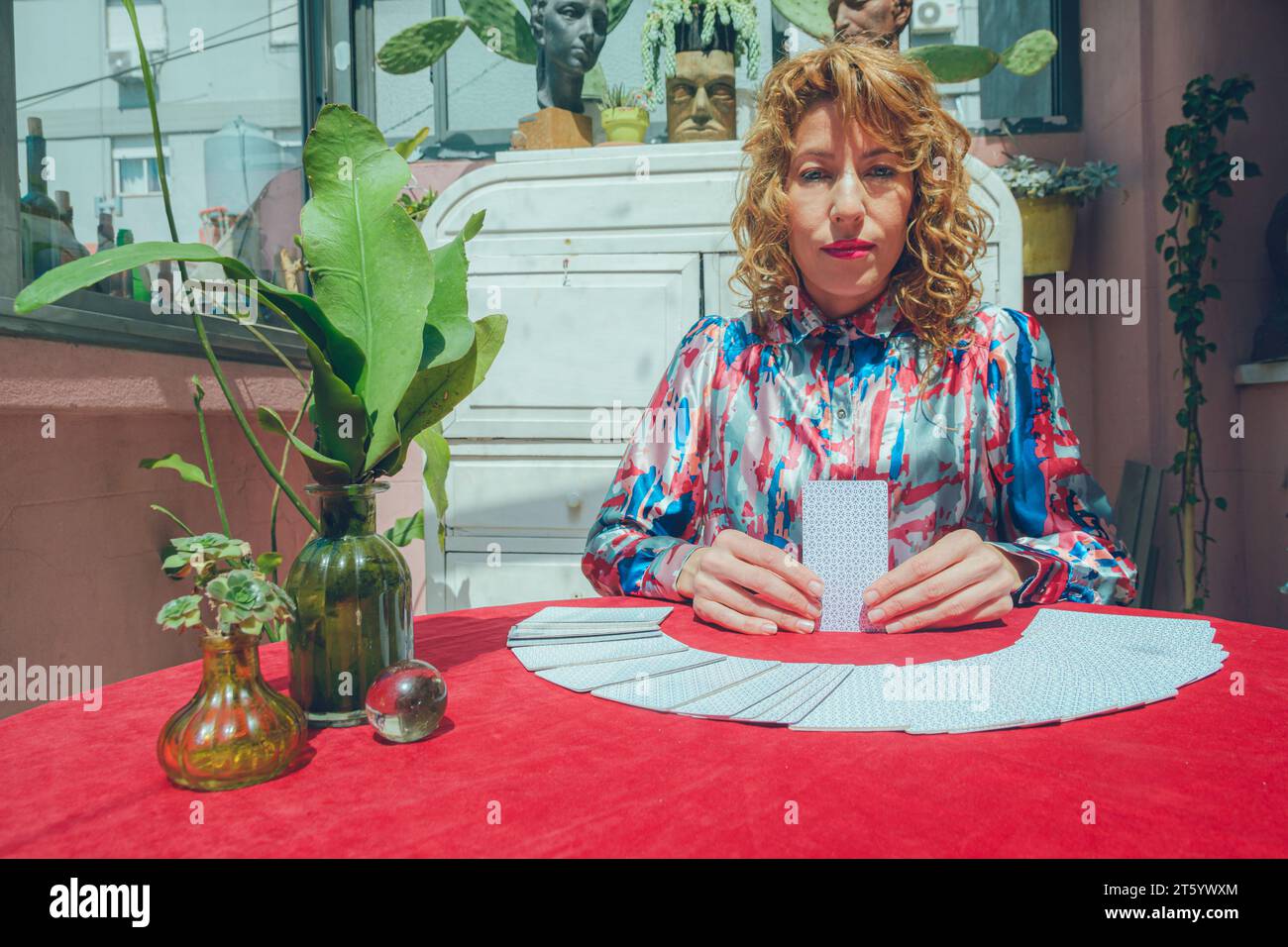 Front view of Caucasian tarot reader woman, sitting at home, in session holding card and looking at camera seriously, people and business concept, cop Stock Photo