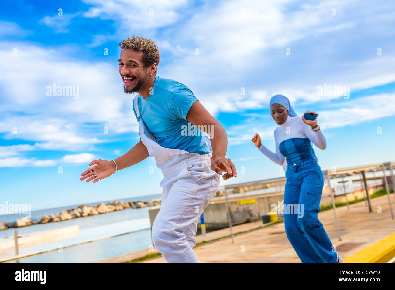 Muslim woman and Mixed-raced man dancing freestyle on the street next to the sea Stock Photo