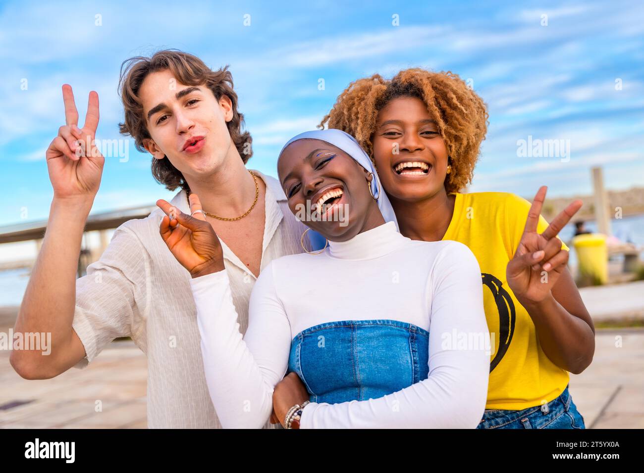 Portrait of three friends gesturing peace while smiling in an urban space Stock Photo