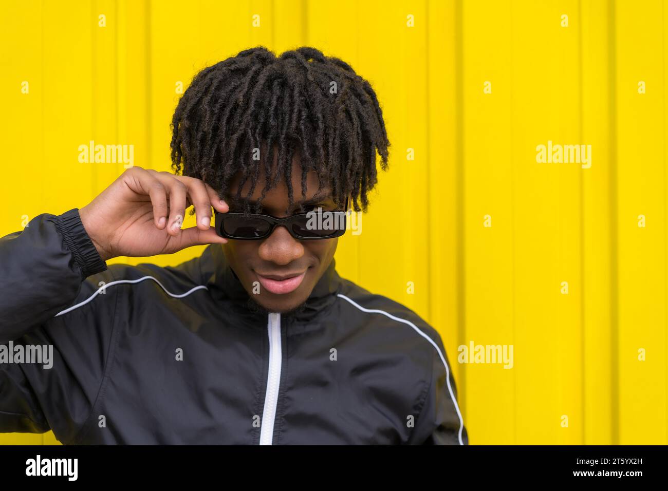 African american young man wearing sunglasses with cool attitude next to a yellow urban wall Stock Photo