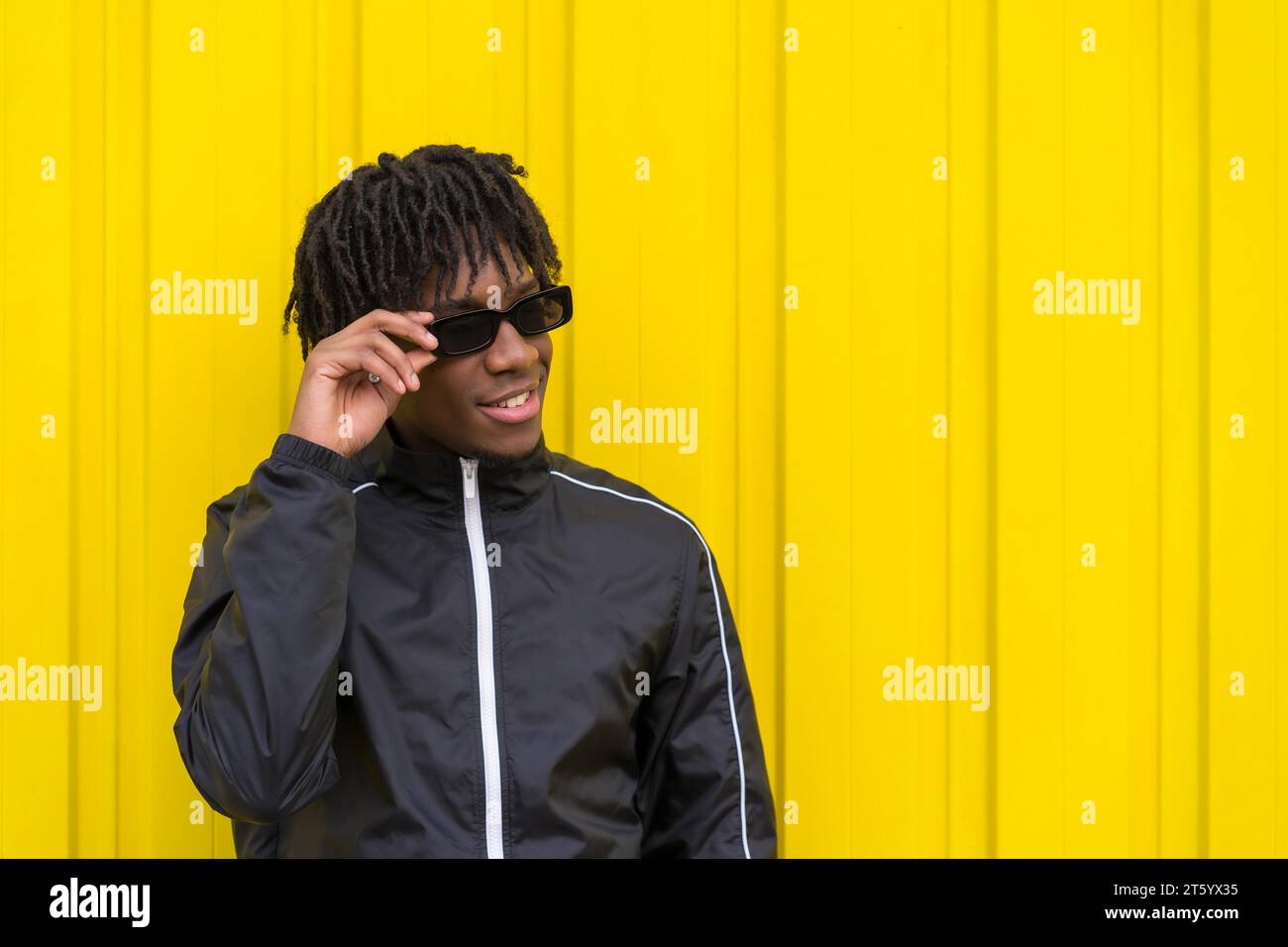 African young man wearing sunglasses with cool attitude next to a yellow urban wall Stock Photo