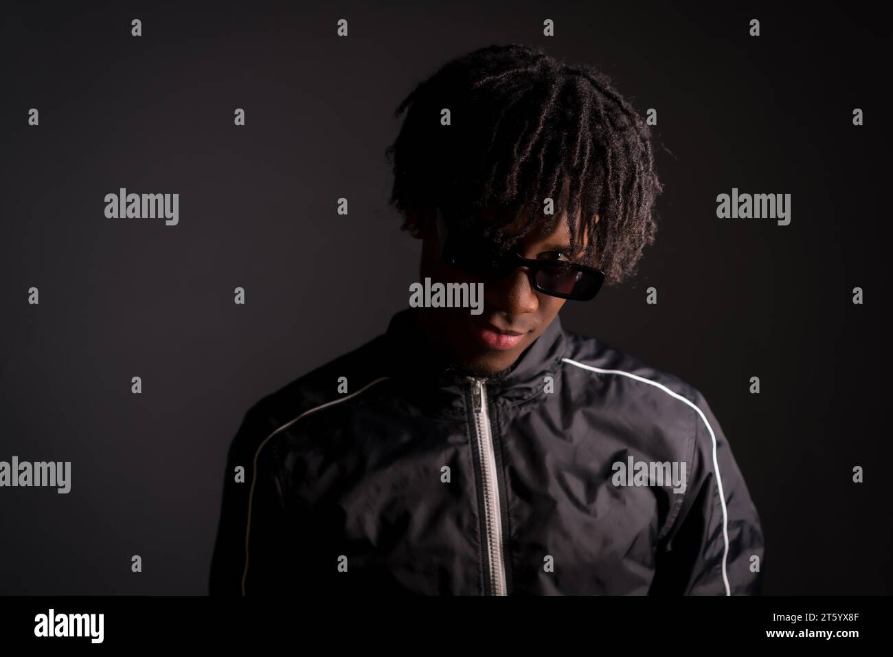 Dark studio portrait of an african cool young man with sportive trendy clothes and sunglasses Stock Photo