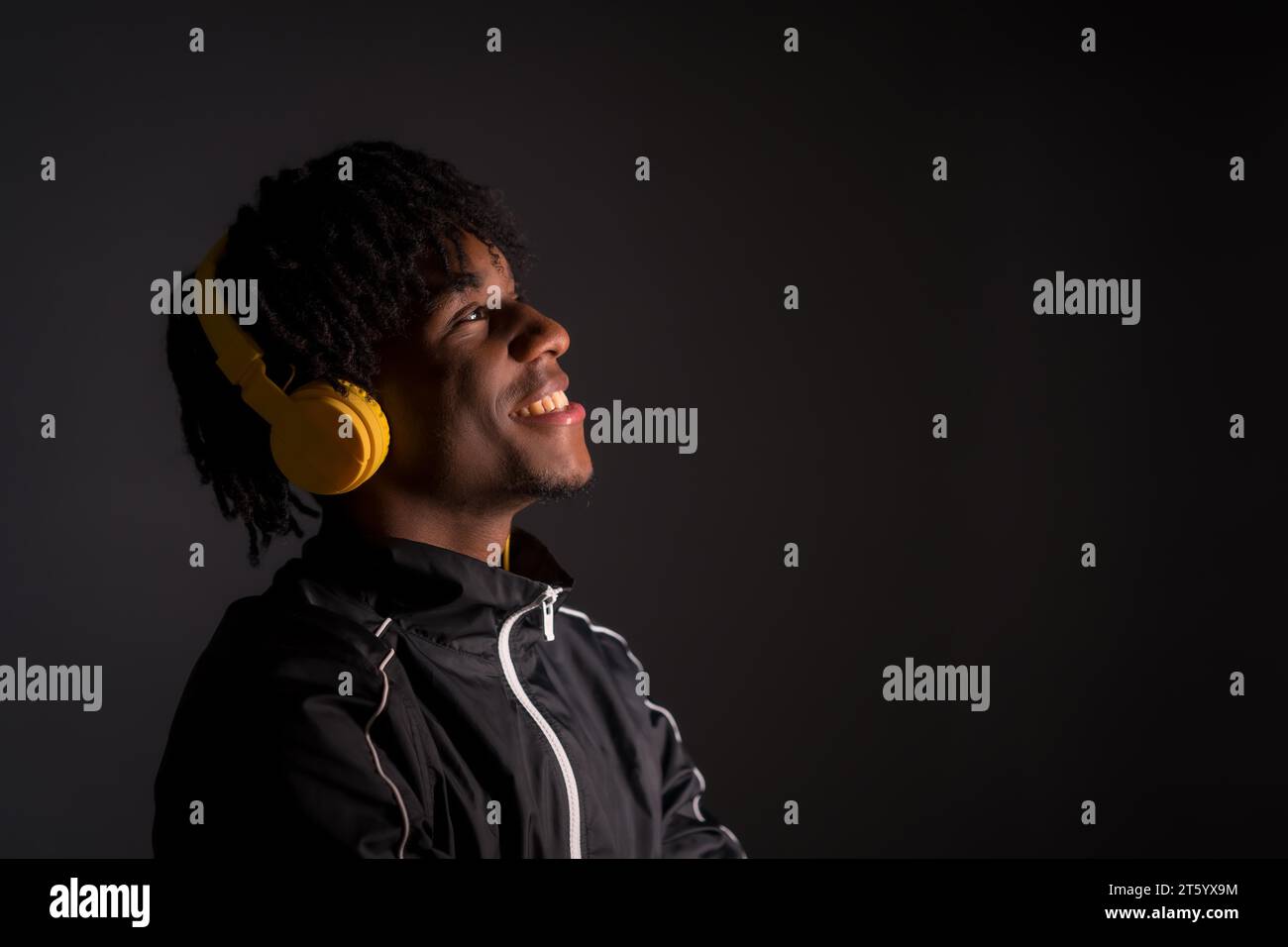 Dark studio portrait of a young african man listening to music with headphones Stock Photo