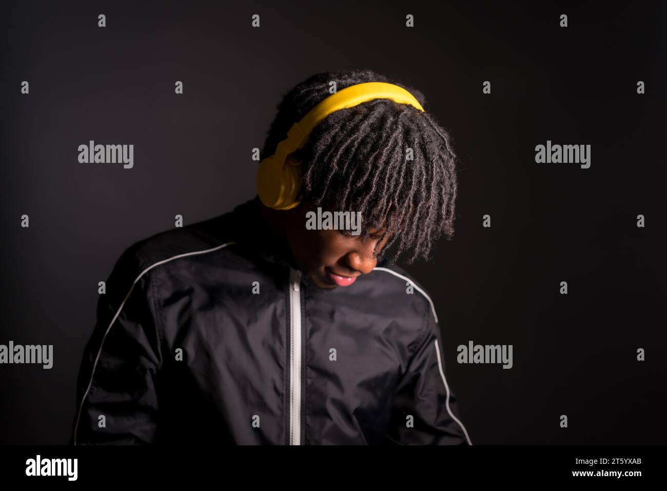 Dark studio portrait of a distracted young african man listening to music with headphones Stock Photo