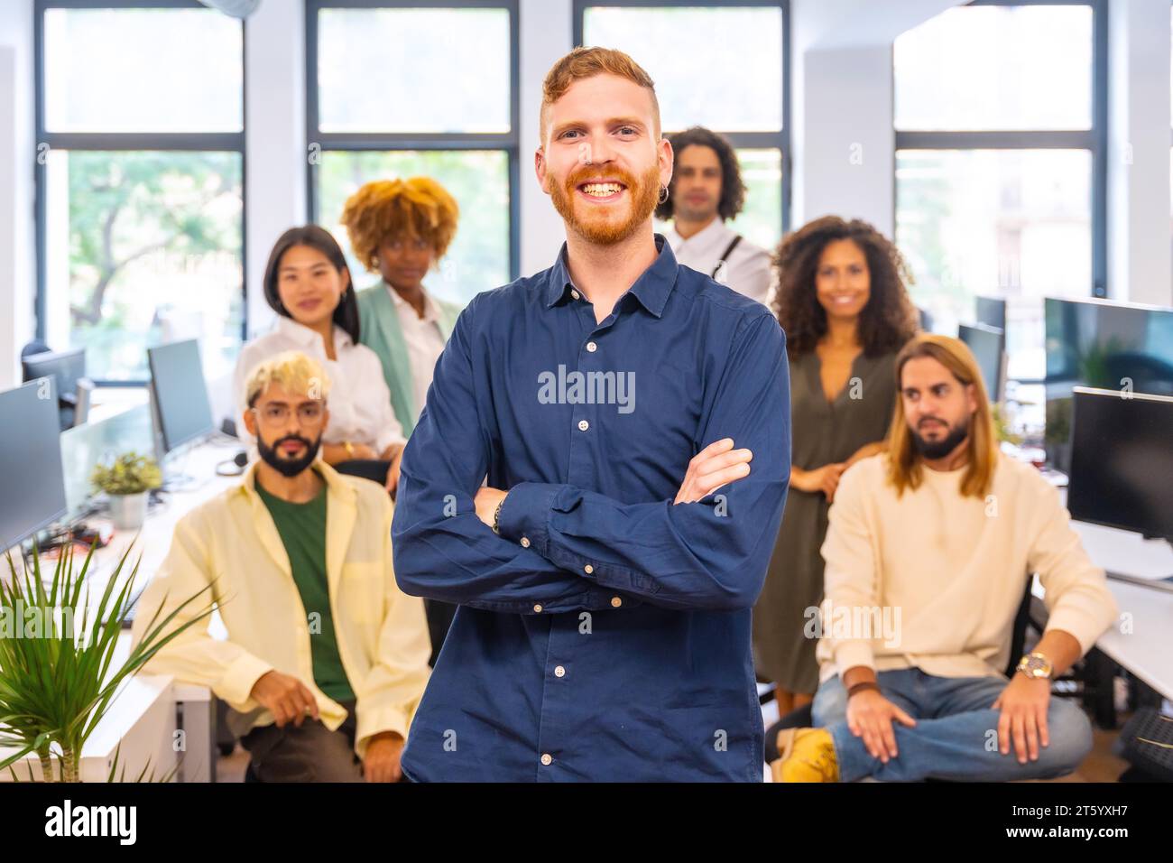 Smiling manager standing proud surrounded by his work team in a coworking Stock Photo