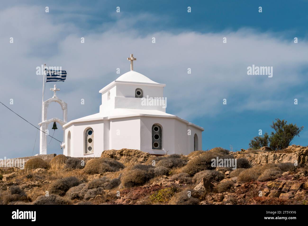 A quaint Greek chapel stands proudly on the cliff's edge, its flag fluttering in the sea breeze, offering a picturesque and spiritual view of Greece's Stock Photo