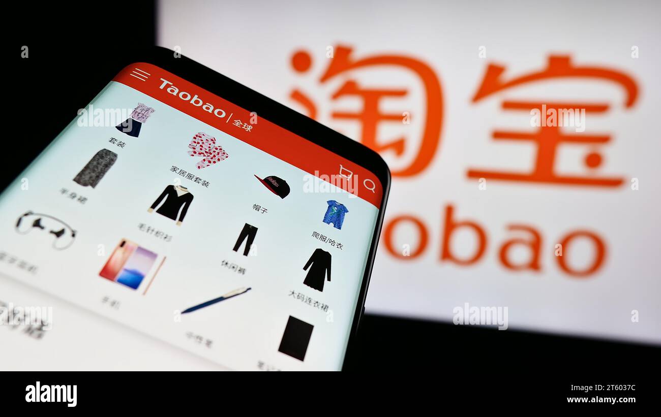 Mobile phone with website of Chinese online shop Taobao (Alibaba Group) in front of business logo. Focus on top-left of phone display. Stock Photo