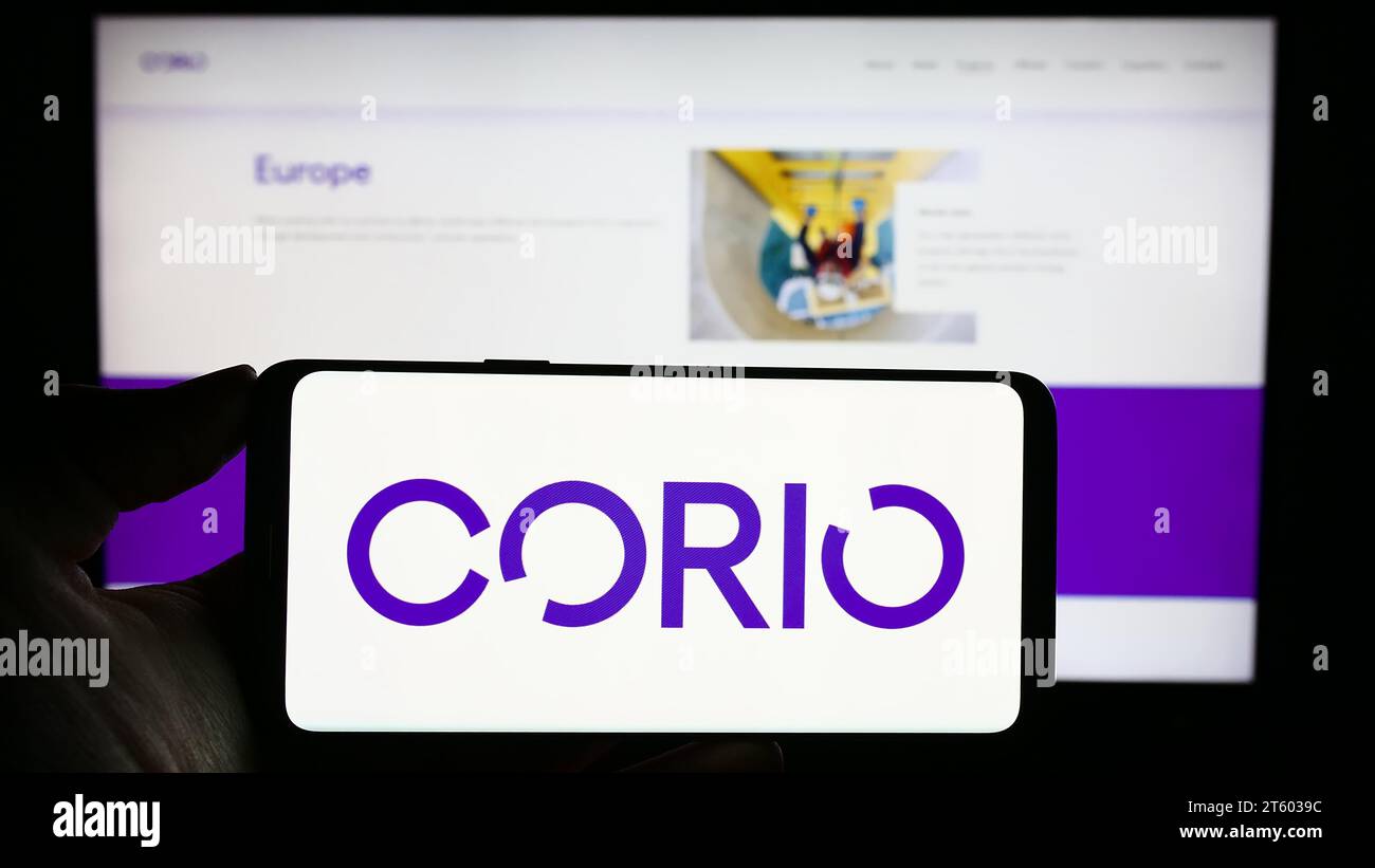 Person holding cellphone with logo of renewables investment company Corio Generation Limited in front of webpage. Focus on phone display. Stock Photo