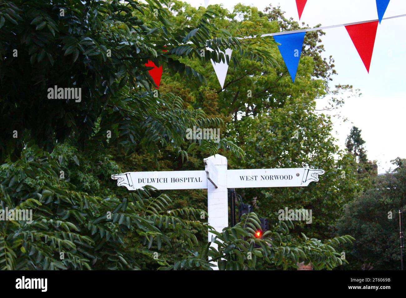 Cute white signs in Dulwich Village, with colorful banners overhead surrounded by greenery Stock Photo