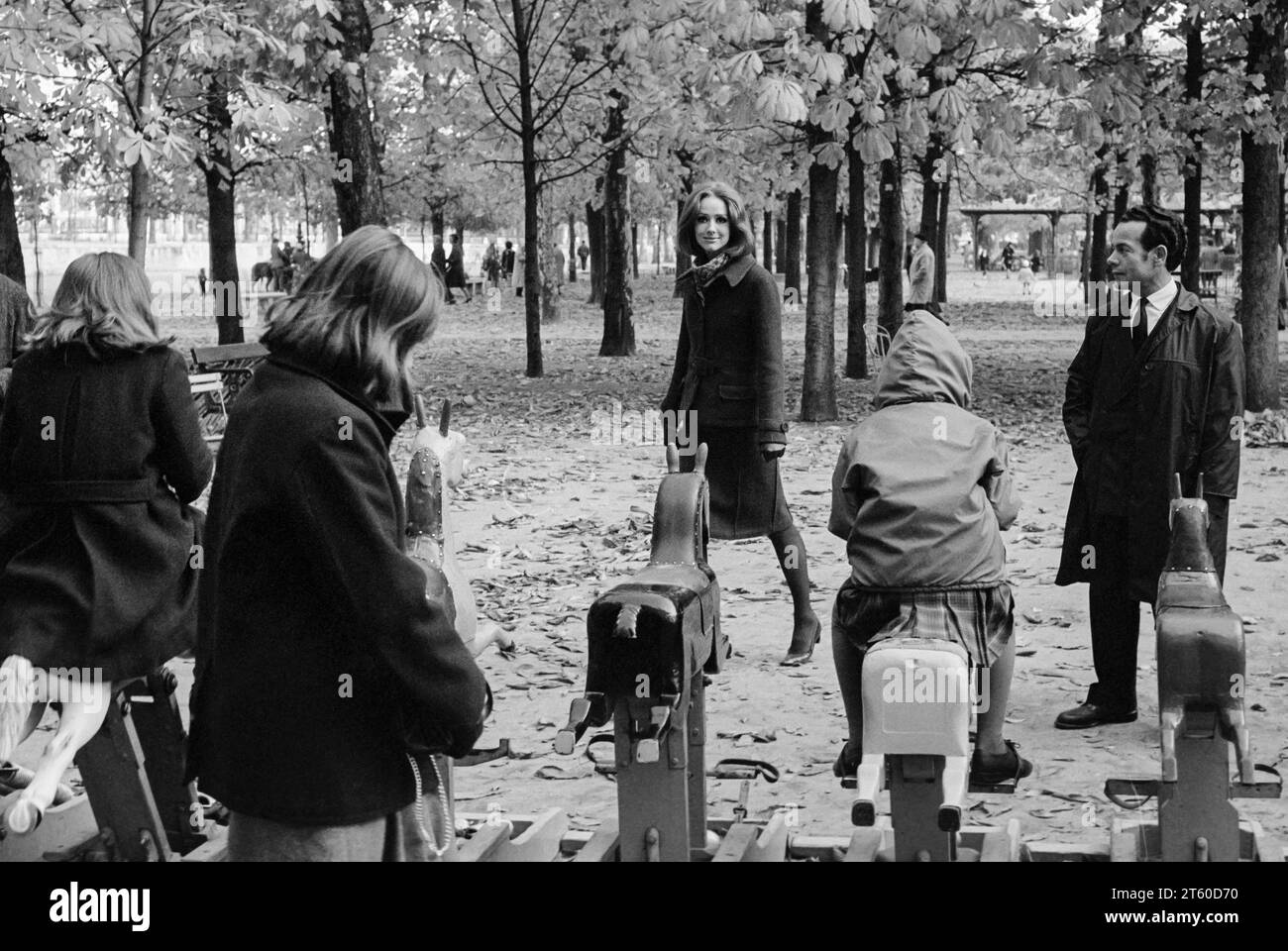 1960s, woman fashion model and man look at children playing on a horse carousel, Jardin des Tuileries garden, Paris, France, Europe, Stock Photo