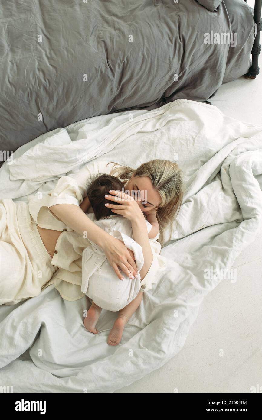 The little girl lay down on her mother and wants to sleep. Mom tenderly  hugs her daughter. Vertical frame Stock Photo - Alamy