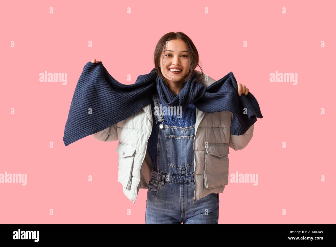 Beautiful young Asian woman in warm scarf on pink background Stock Photo