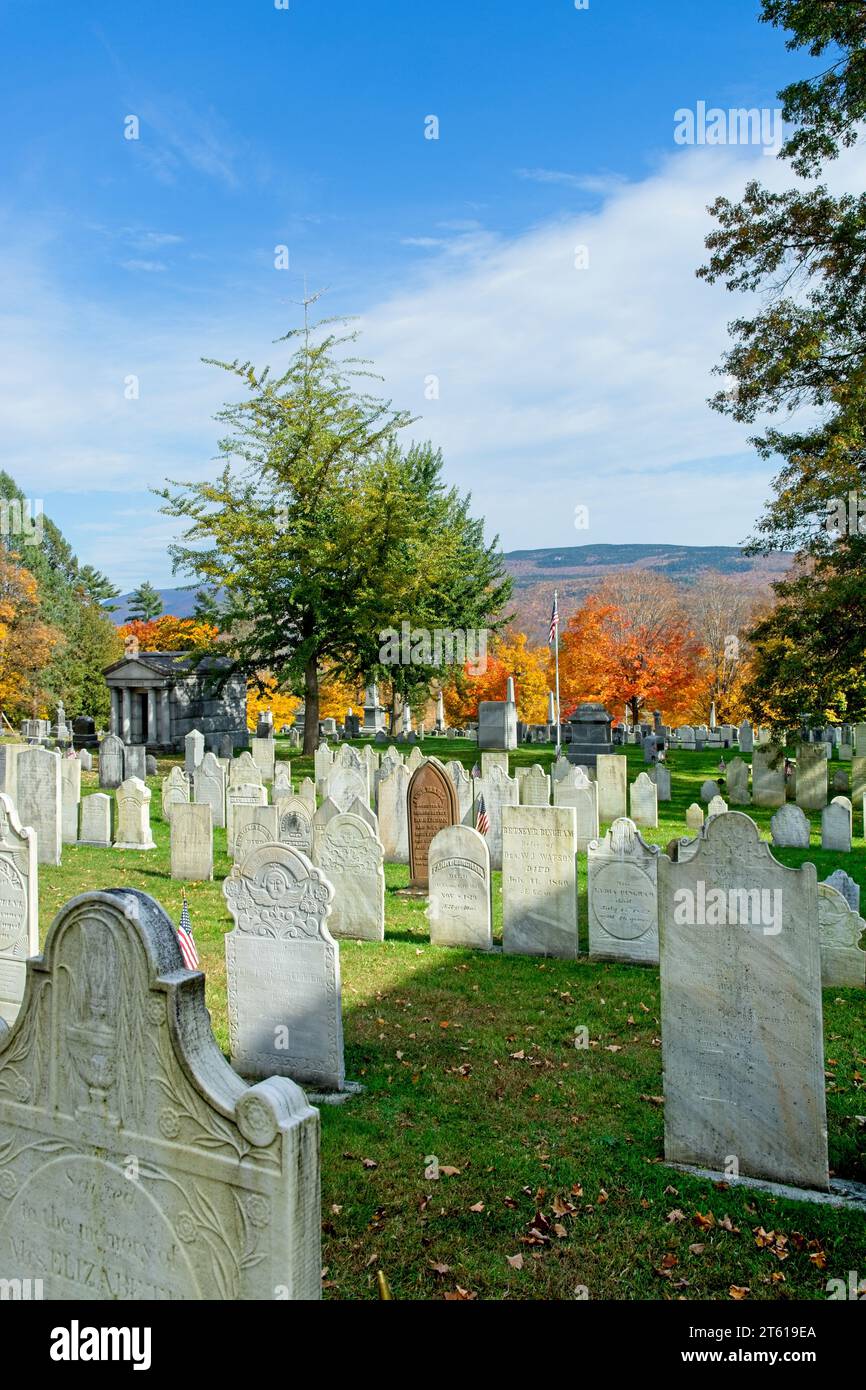 Rows of headstones dot the lawn of 1806 Old First Congregational church cemetery distant hillside covered in autumn leave colors in Bennington Vermont Stock Photo