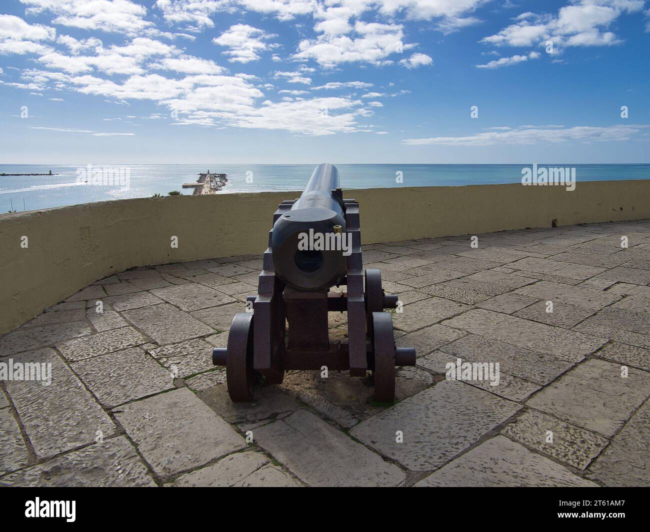 Iron Cannon Pointing Towards the Vast Ocean Horizon with blue sky. Historic cannon on iron wheels. Stock Photo