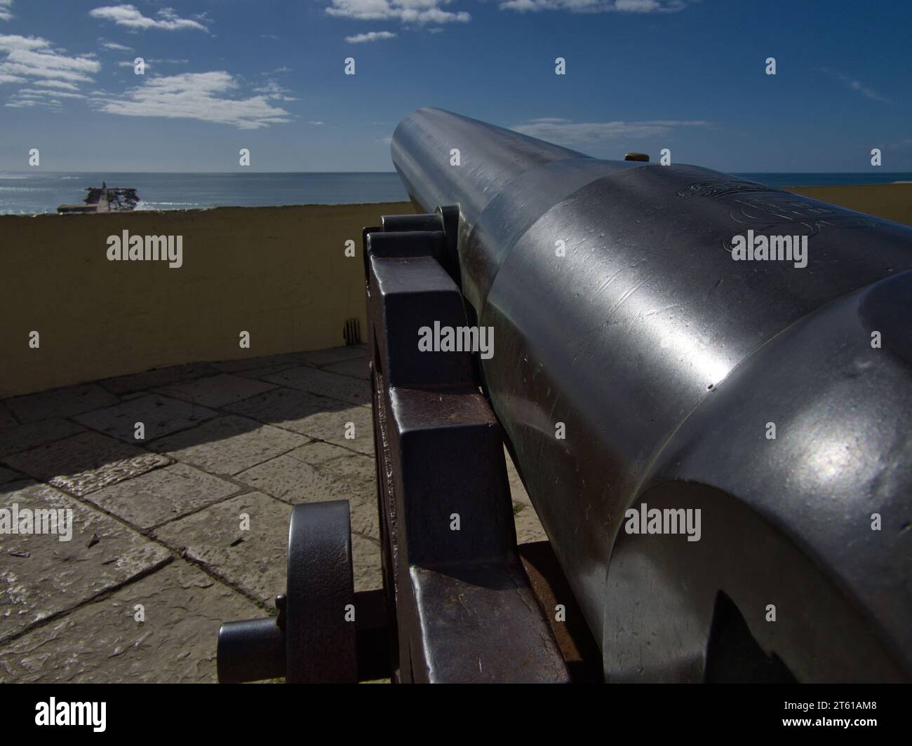 Iron Cannon Pointing Towards the Vast Ocean Horizon with blue sky. Historic cannon on iron wheels. Stock Photo