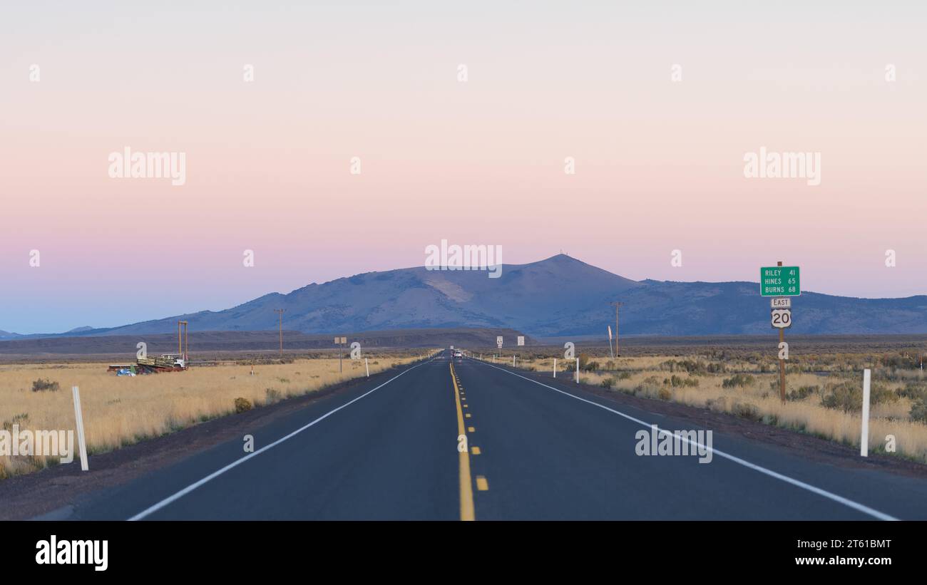 Long straight stretch of US highway 20 in central Oregon crossing the High Desert at dusk with distant mountain on horizon Stock Photo
