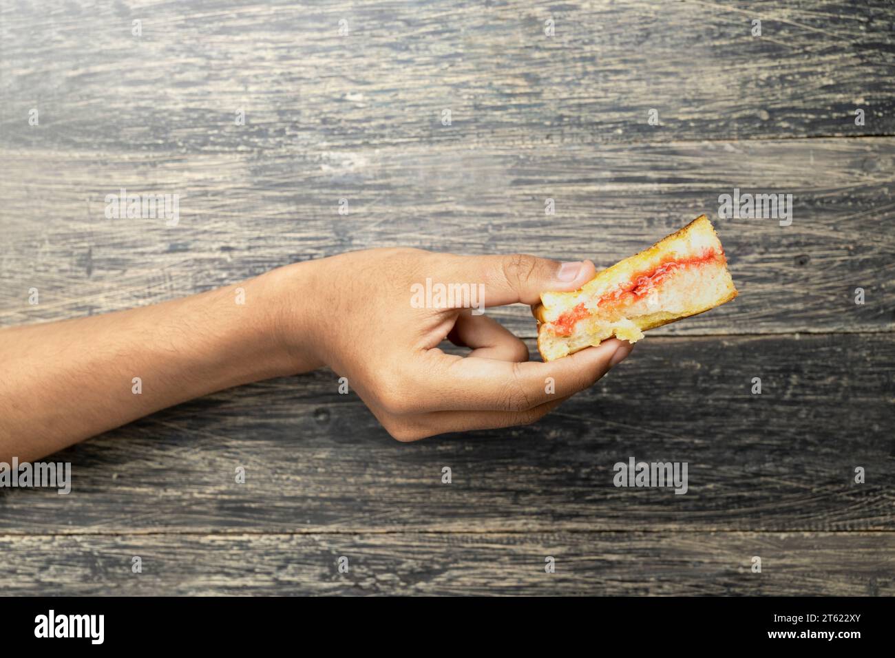 Human hand holding roasted bread (Roti Bakar) with strawberry jam. Traditional Indonesia food Stock Photo