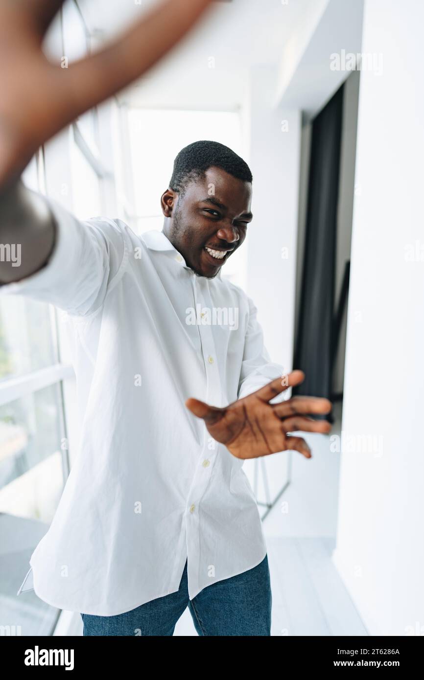 Young african man in white shirt and glasses posing near large window ...