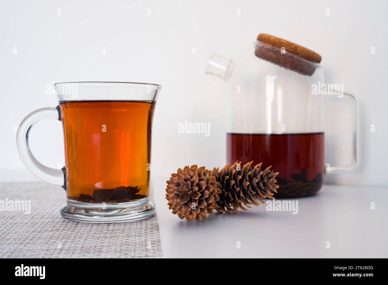 Black tea in a glass cup and glass teapot freshly brewed on a napkin and pine cones with white background Stock Photo