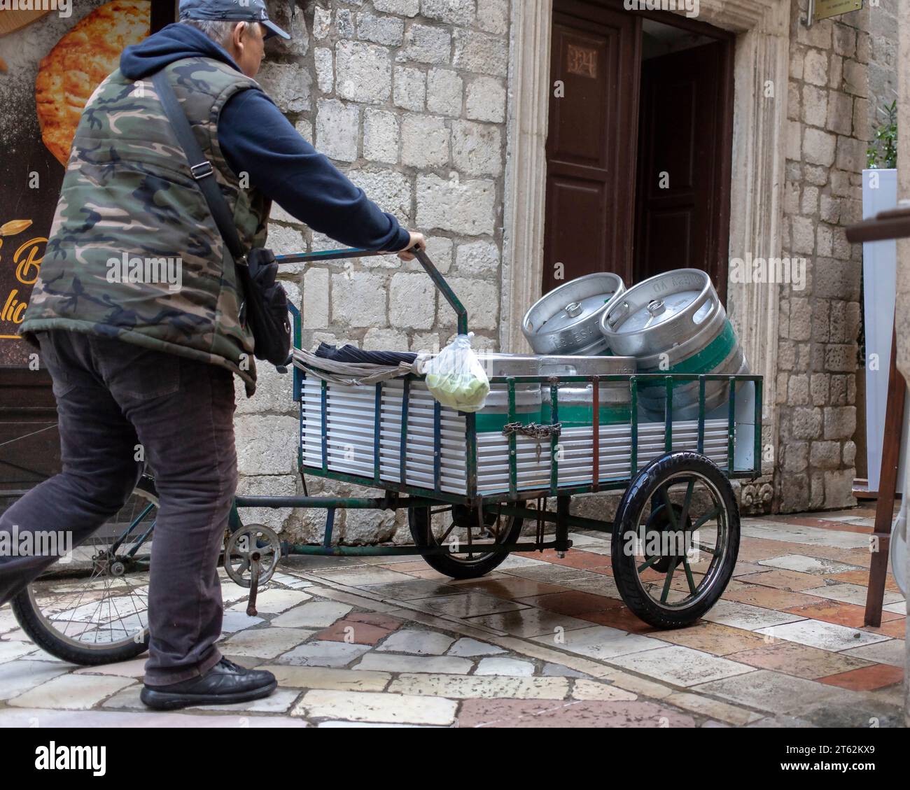 Montenegro, April 15, 2023: Man pushing a delivery tricycle loaded with beer kegs down the narrow cobblestone street of Kotor Old Town Stock Photo
