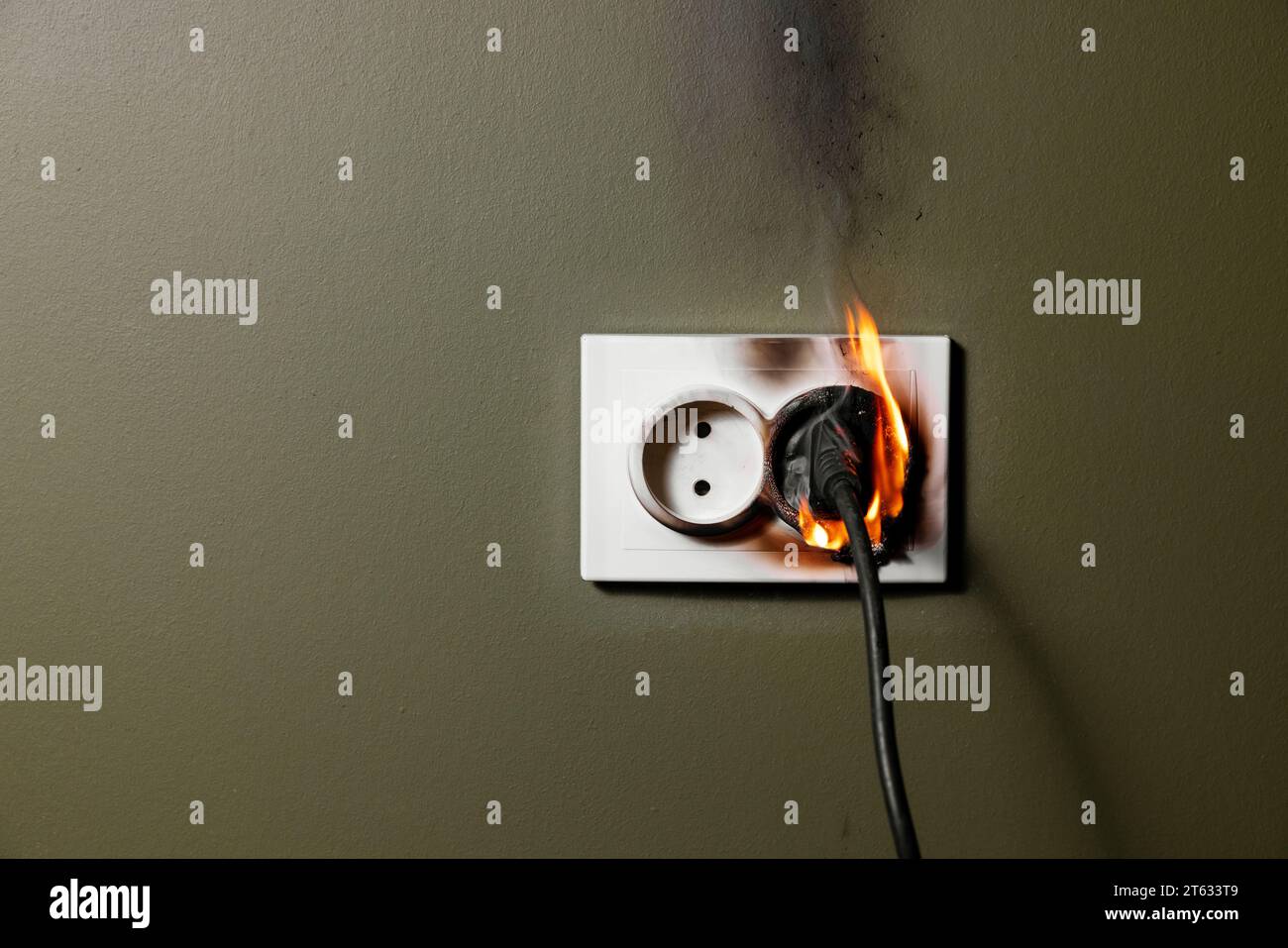 burning wall electrical socket with plugged appliance cable from short circuit in house. concept of fire safety and power overload at home Stock Photo