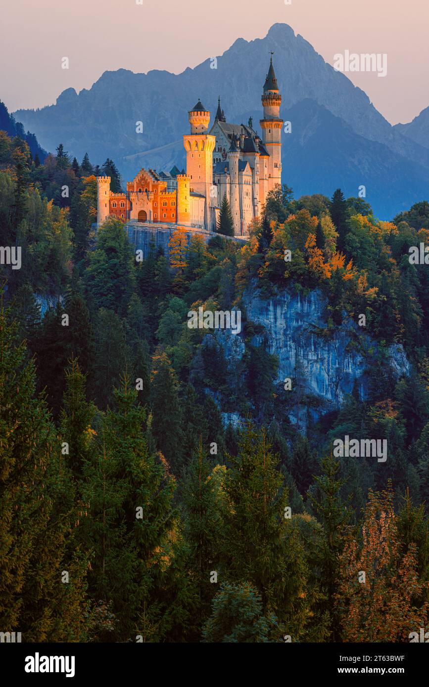 Neuschwanstein Castle illuminated after sunset surrounded by autumn colours, located close to the town of Füssen, in the Allgäu, in Bavaria, southern Stock Photo