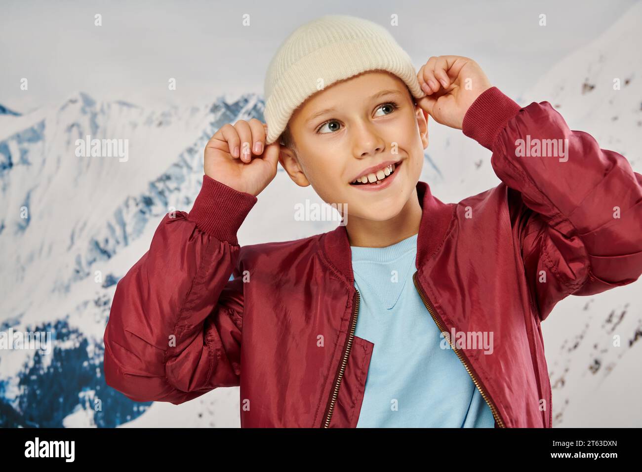 cheerful little boy in stylish attire putting on his trendy beanie hat looking away, fashion