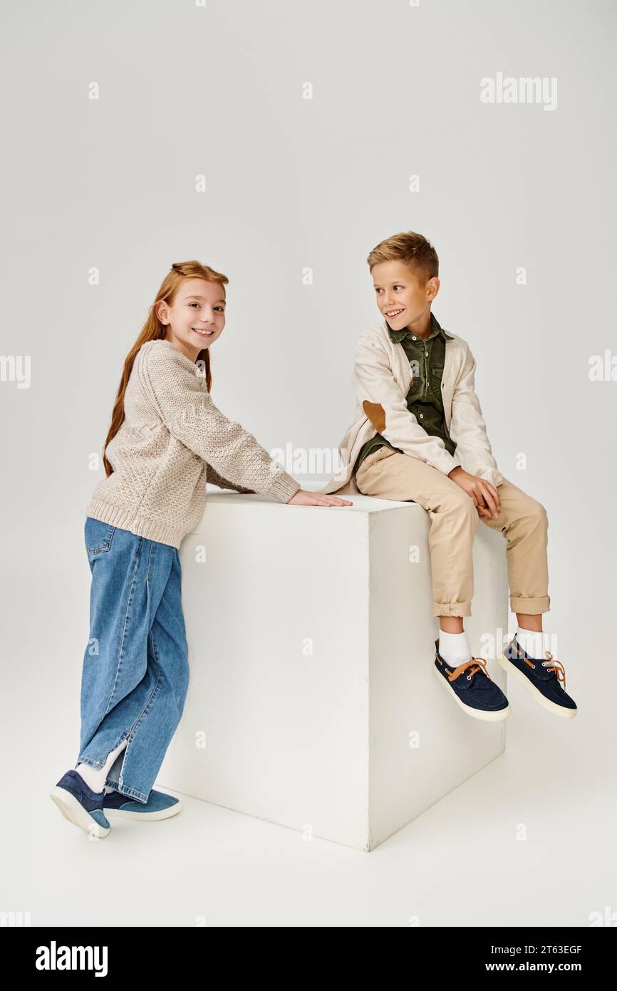 cheerful little boy in cardigan smiling at preteen red haired girl that looking at camera, fashion Stock Photo