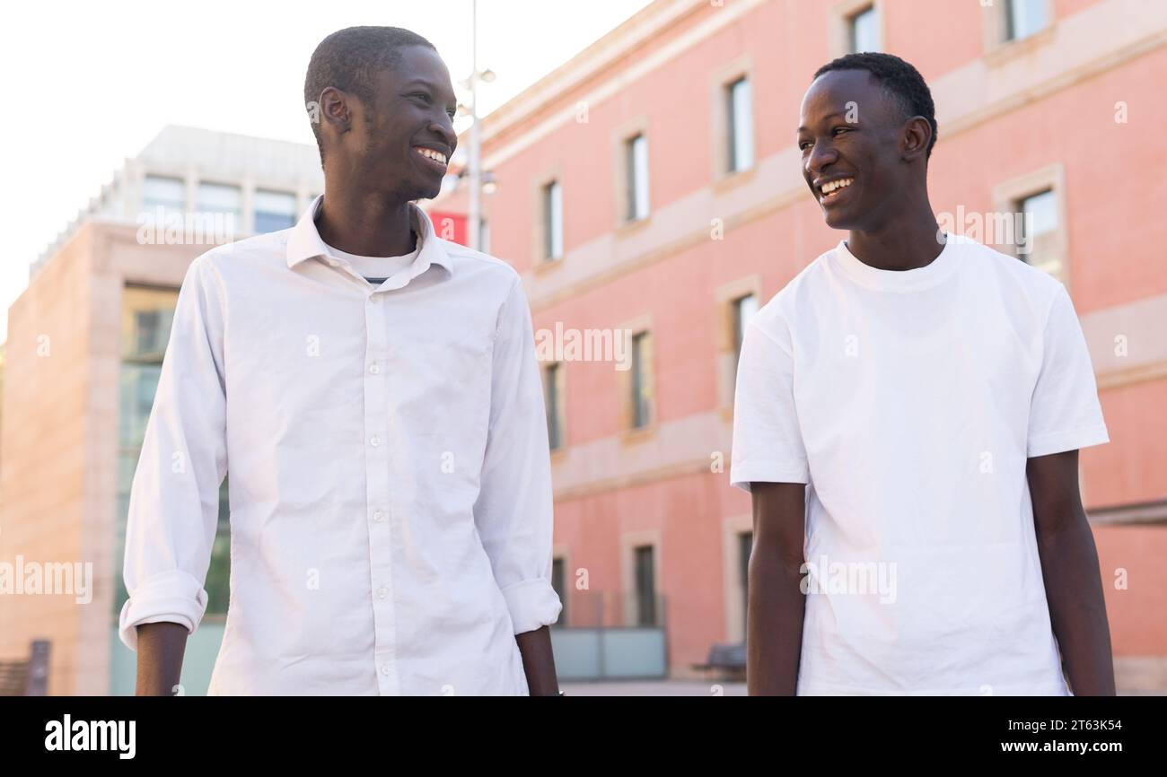 Happy two African American young men sharing a light moment against an urban backdrop looking at each other Stock Photo
