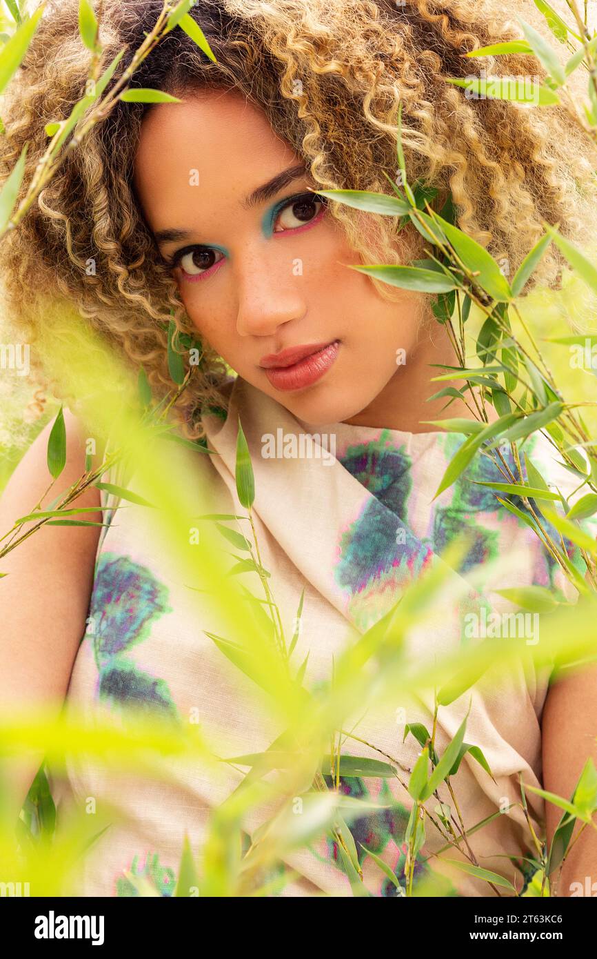 Closeup of ethnic young woman with curly blonde hair stands amidst tall ...
