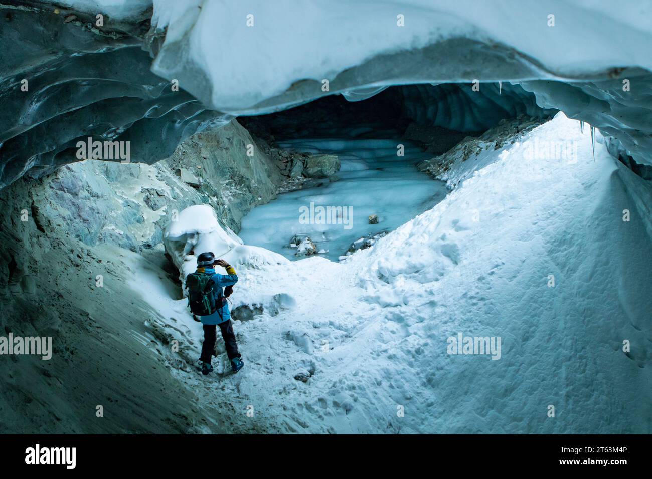 From below of unrecognizable person taking a photo in cave at snowy mountain while exploring during vacation at Swiss Alps Stock Photo