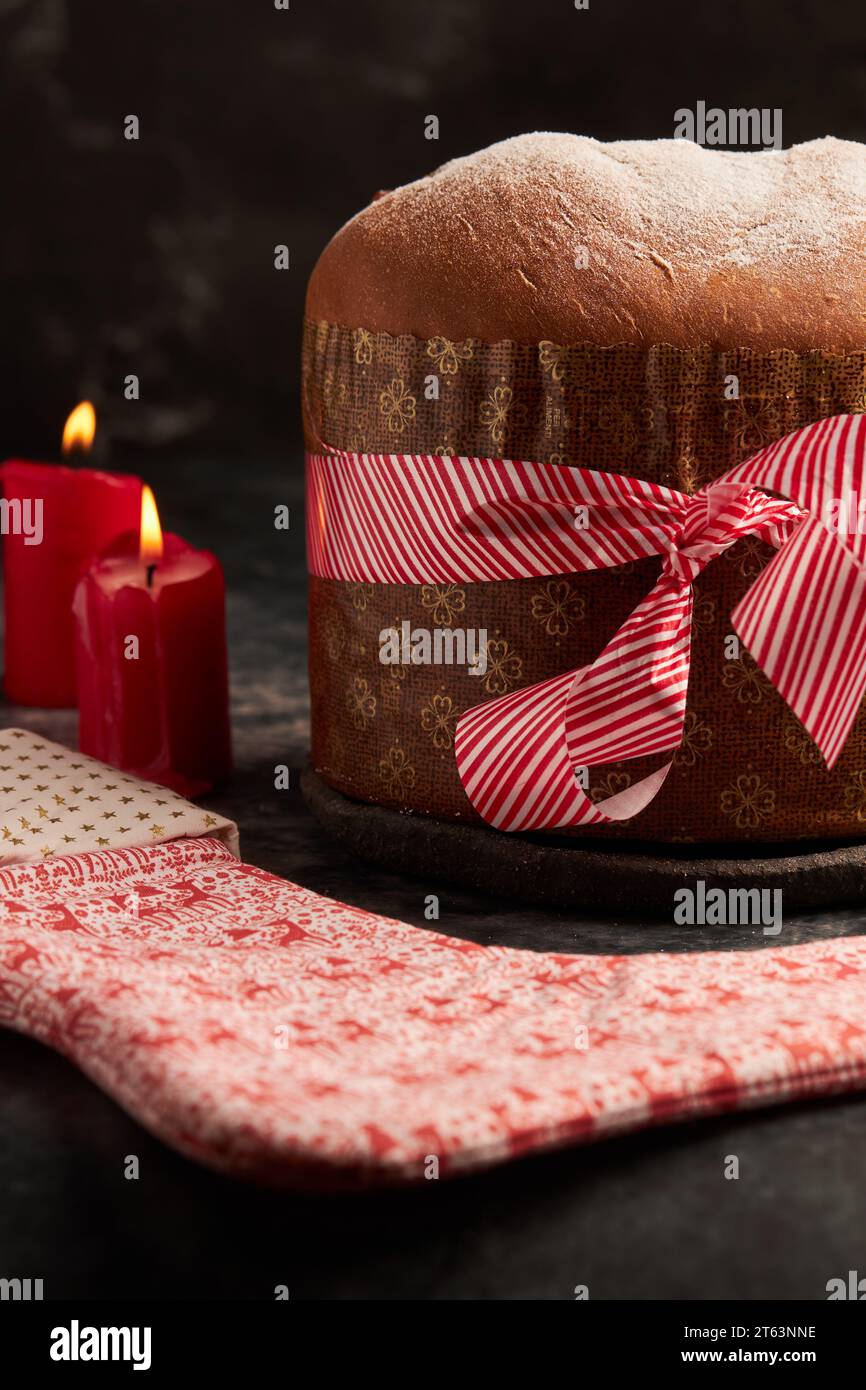 A beautifully presented panettone bread wrapped with a striped red ribbon, accompanied by a decorative fabric with festive patterns, set amidst ambien Stock Photo