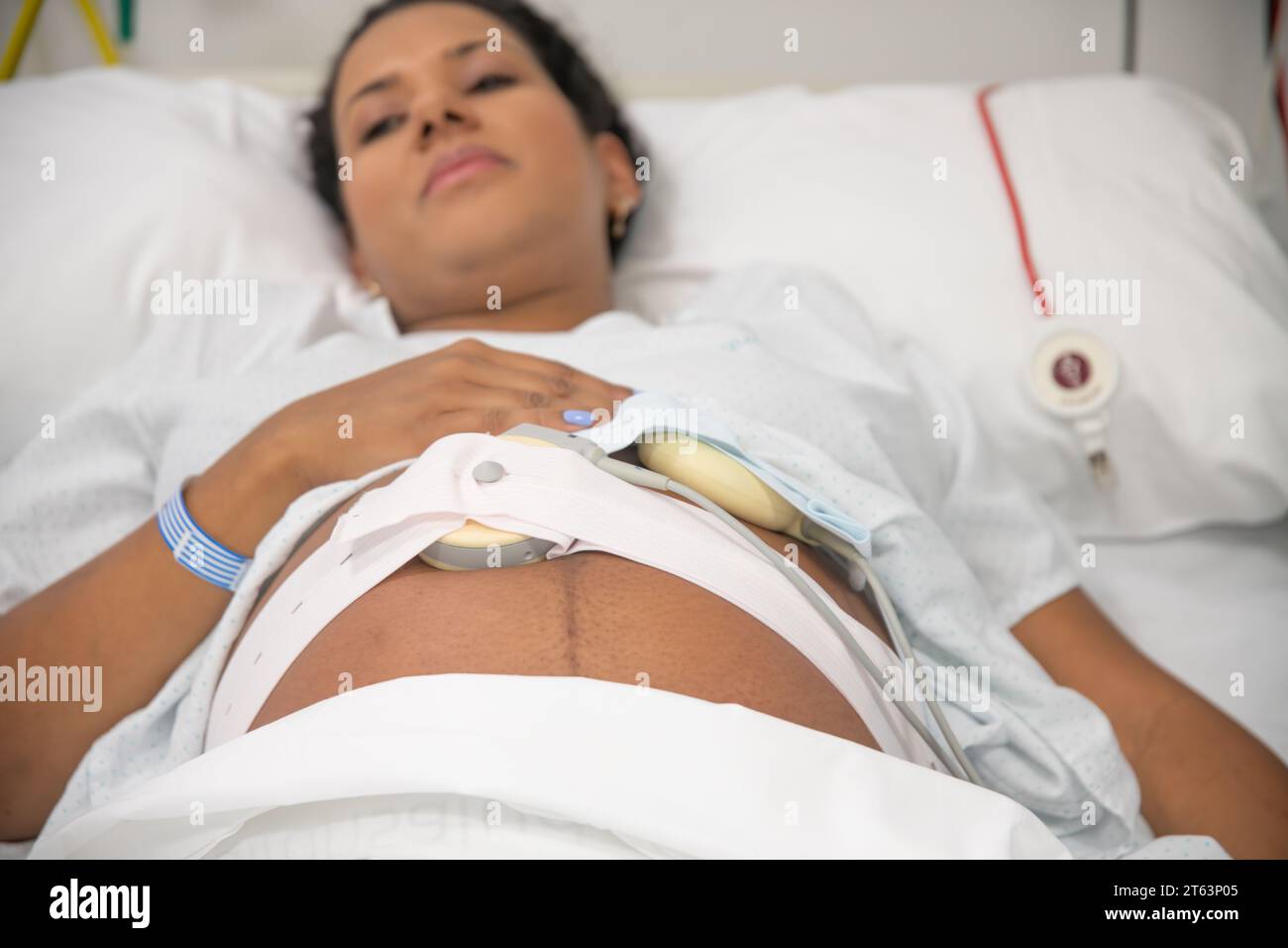 Closeup of an expectant mother in a hospital bed, touching her belly with a fetal heart rate