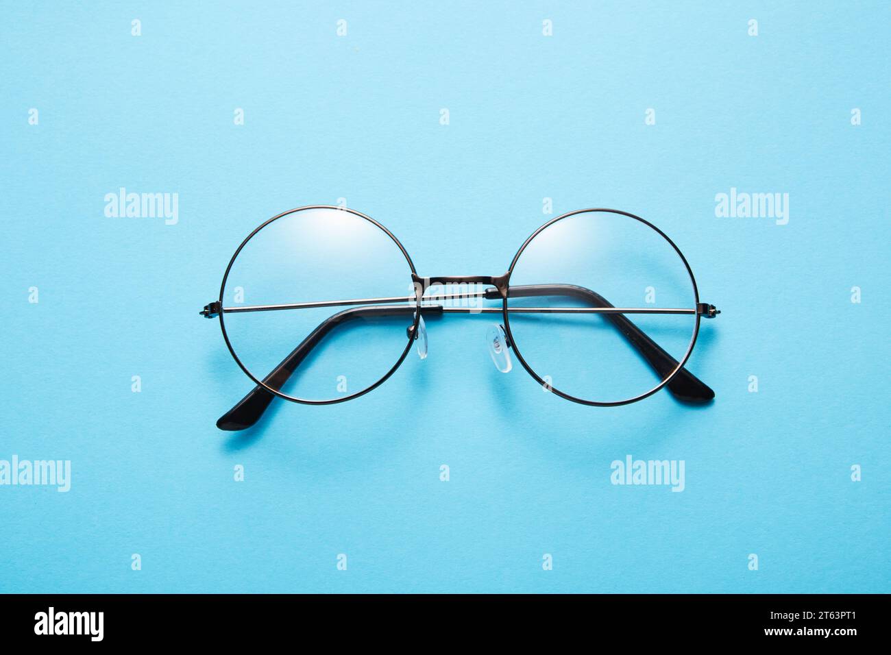 Glasses in round thin metal frame isolated on blue surface. Stock Photo