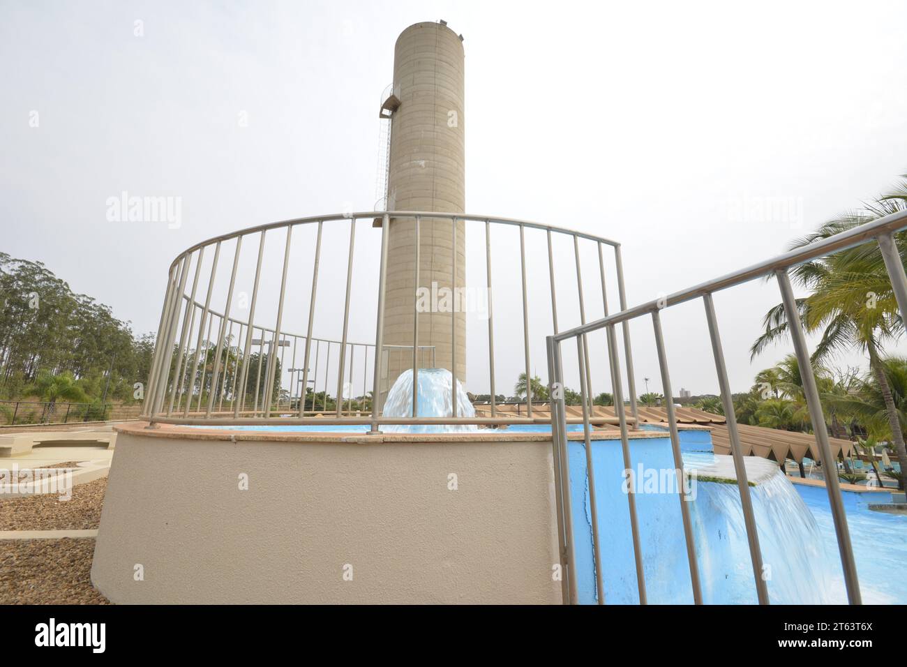 Geyser in a pool with guardrails and a concrete tower in the background ...