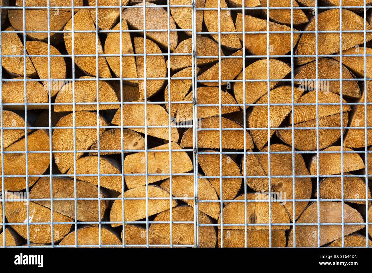 Wooden firewood logs are stacked behind metal mesh. Wood texture and