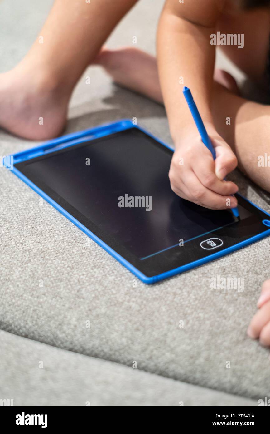 Child drawing with a blue pen on an electronic black board surface tablet Stock Photo