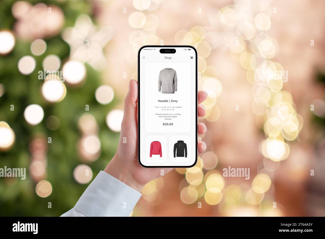 Woman's hand holds a mobile phone with a modern e-commerce app, engaged in Christmas shopping. Festive bokeh of Christmas tree lights creates a holida Stock Photo