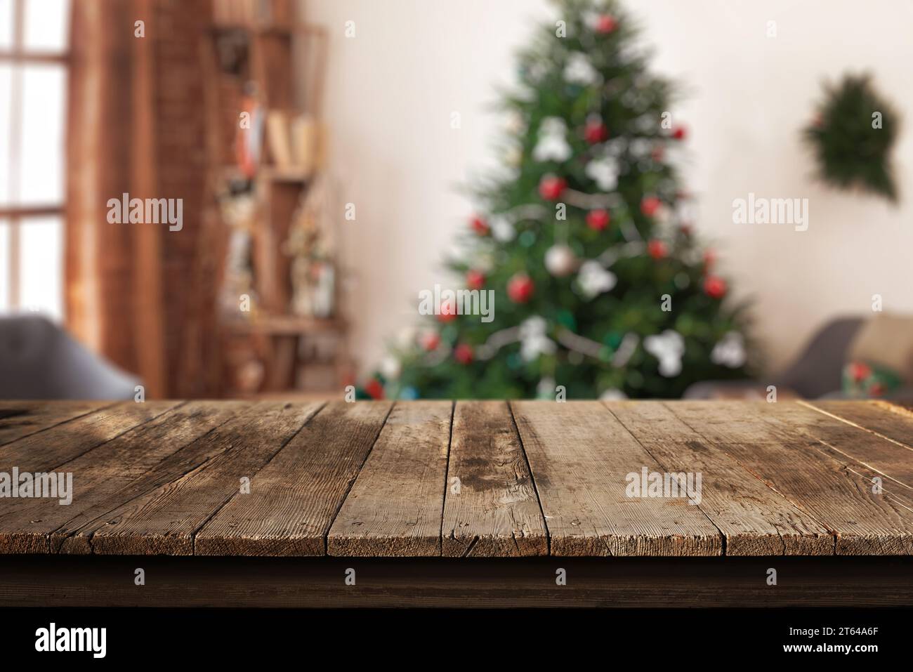 Wooden desk in a home living room with a Christmas tree and festive decorations in the background. Perfect setting for a warm and inviting holiday atm Stock Photo