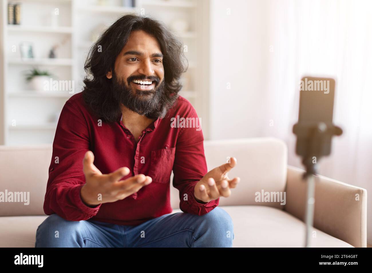 Indian guy vlogger streaming from home, using phone on tripod Stock Photo