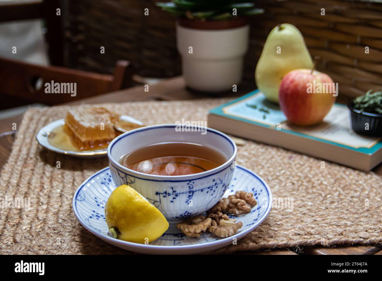 Morning setup on wooden table at balcony, books to read, cup of natural tea, teapot, organic honey from farm, fresh green tea leaves and organic fruit Stock Photo