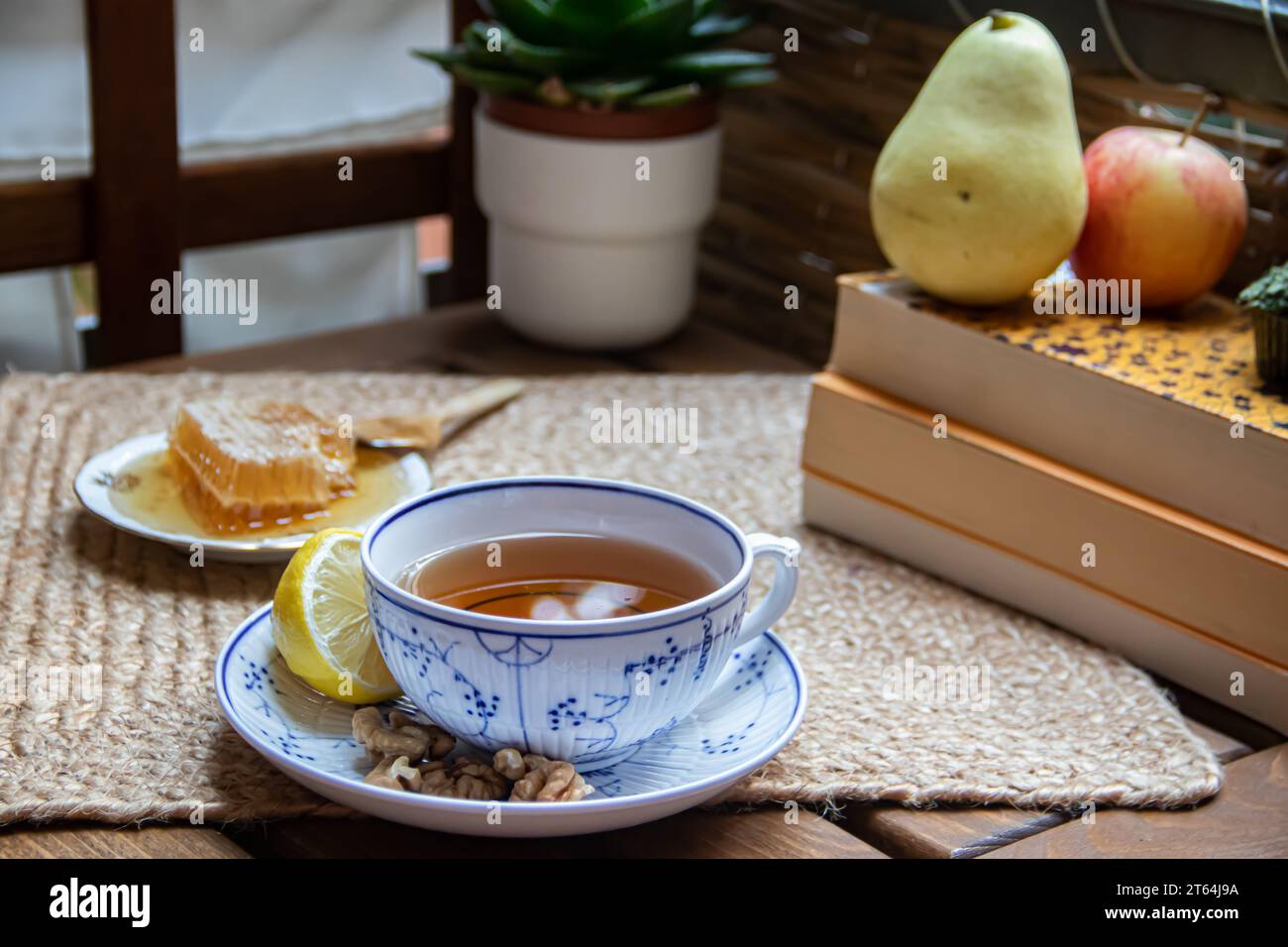 Glass teapot and thermo cup with green tea and dried apricots on wooden  table against defocused sofa with pillows. Front view. Mock-up Stock Photo