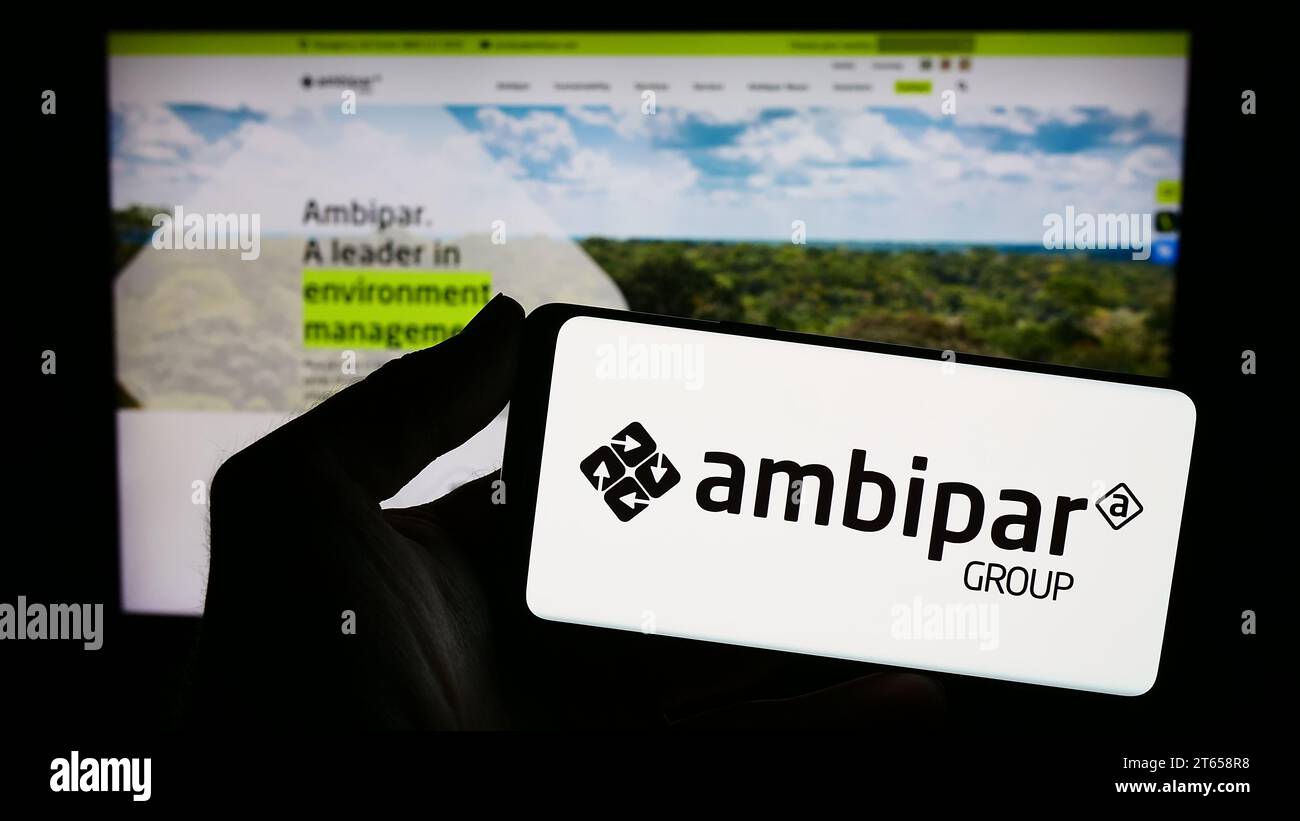 Person holding smartphone with logo of Brazilian environmental services company Ambipar Group in front of website. Focus on phone display. Stock Photo